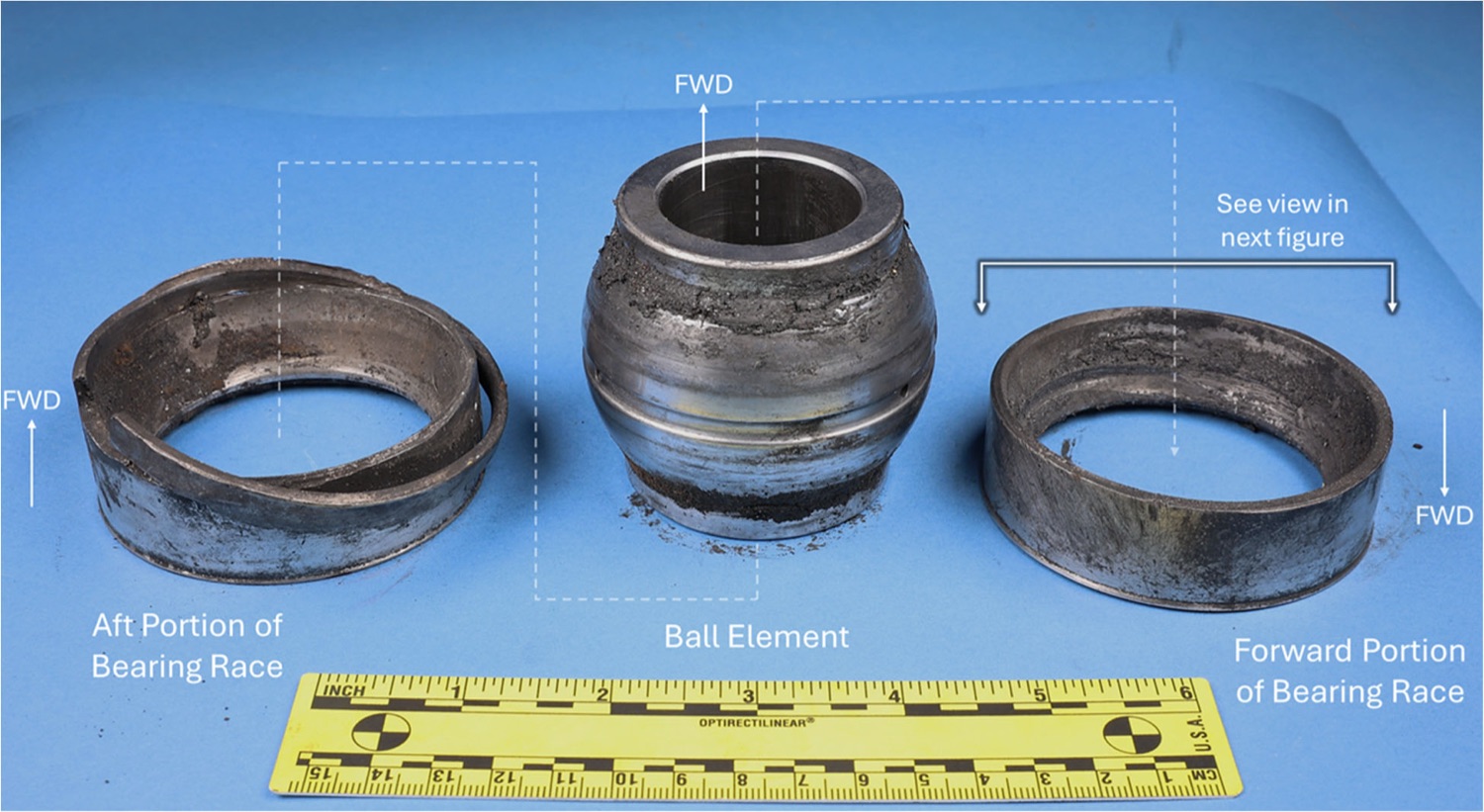 The fractured spherical bearing from the left pylon aft mount, photographed with an evidence scale